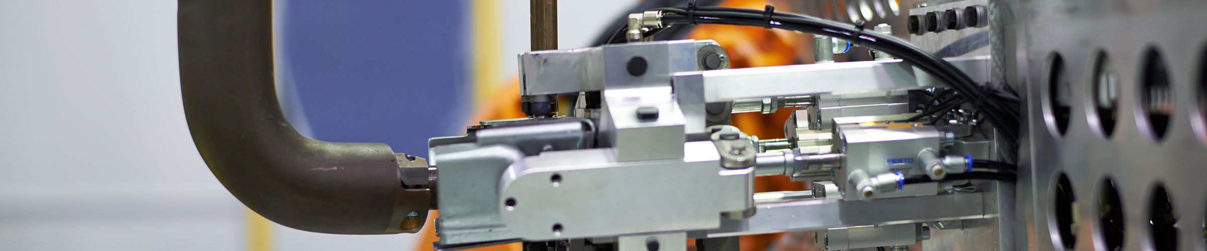 Teil einer Vorrichtungsbau-Vorrichtung: massiver Metallträger mit kreisförmigen Bohrungen, darauf montierte pneumatisch-mechanische Aktoren und Verbindungselemente; im Vordergrund ergonomischer Handgriff – typisches Modul im Sondermaschinenbau.