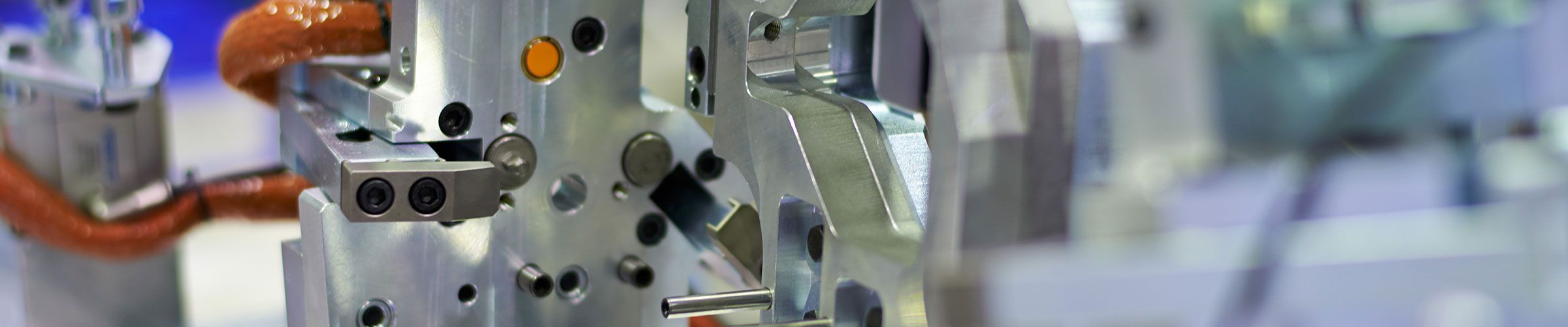 Stabile Vorrichtungsbasis aus Metall: länglicher Träger mit präzise gefrästen Bohrungen und formgenauer Oberfläche, montiert mit mehreren mechanischen Komponenten, Verbindungselementen und rot isolierten Kabeln – typisches Bauteil im Sondermaschinenbau.