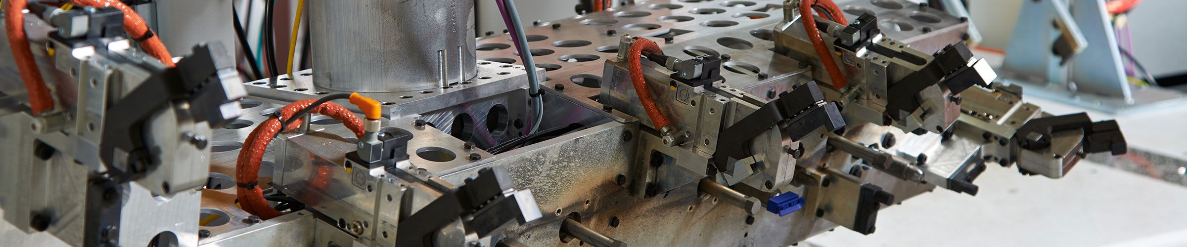 Vorrichtung im Werkzeugbau: länglicher Träger mit präzisen Bohrungen, darauf montierte Bauteile mit Steckverbindungen, Kabeln und Schutzkappen, genutzt für den Sondermaschinenbau.